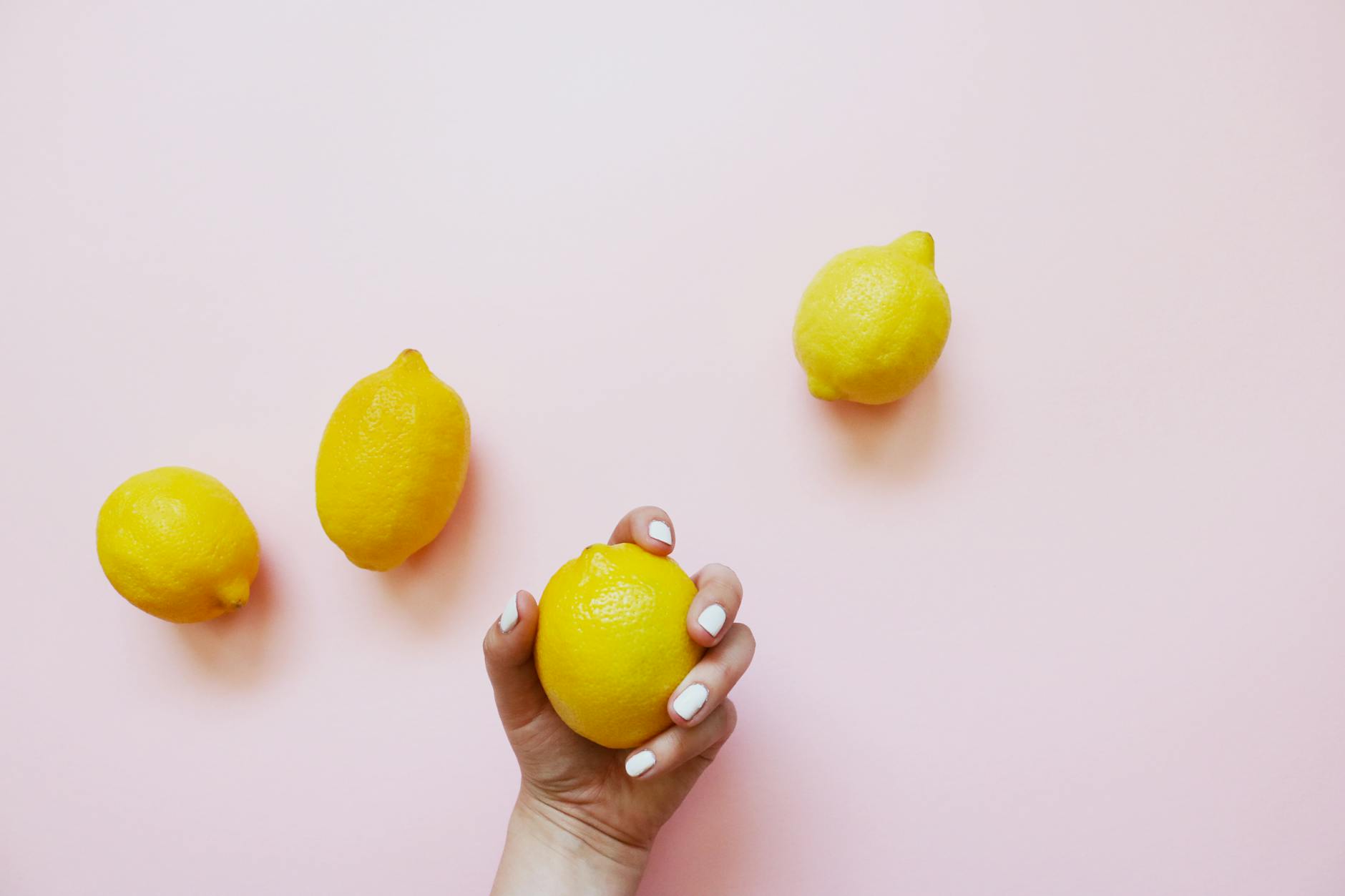 Hand holding a lemon on soft pink background, symbolizing sensitivity and delicate tissue