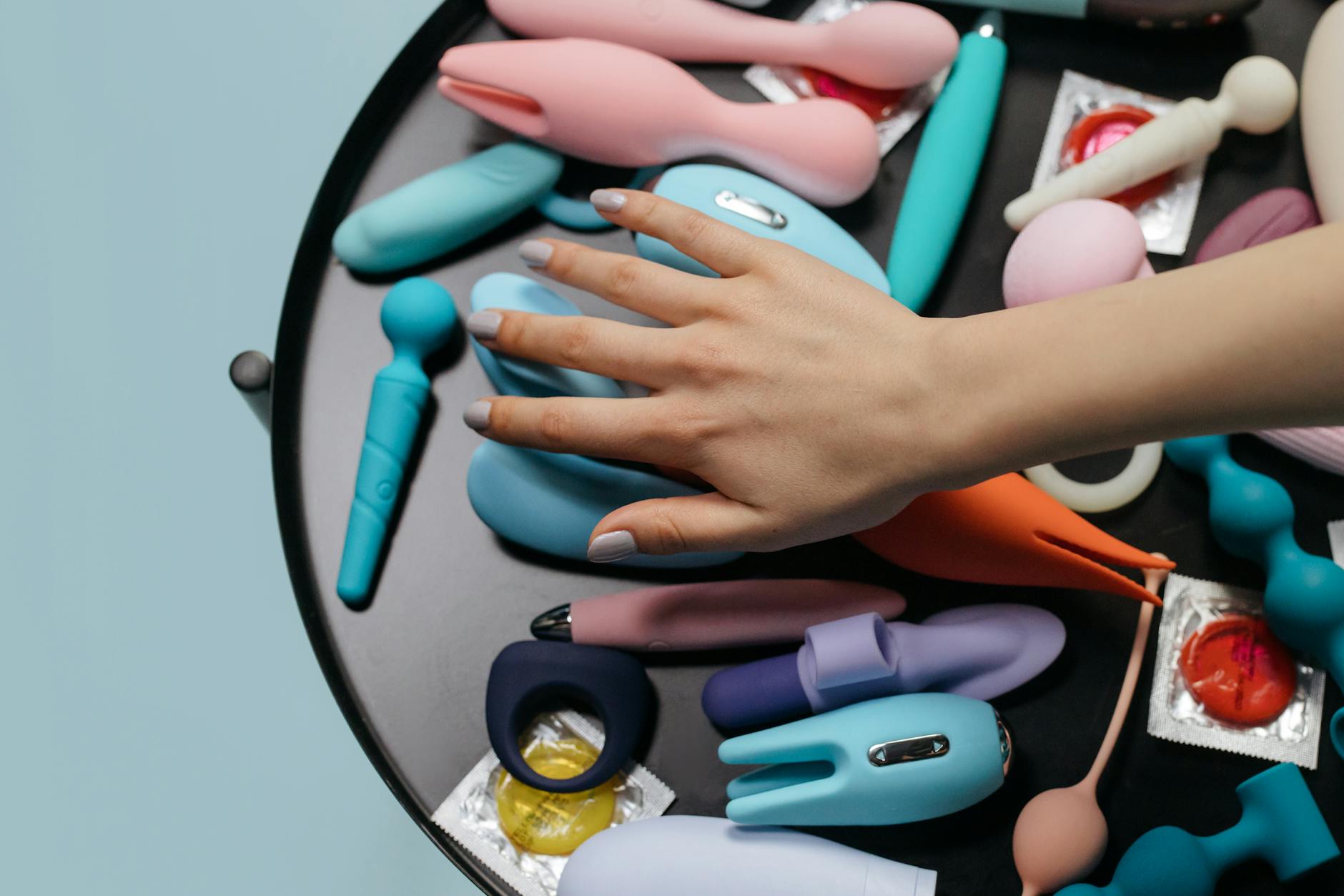 A hand holding a bright blue clitoral vibrator against a neutral background, representing accessible pleasure technology.