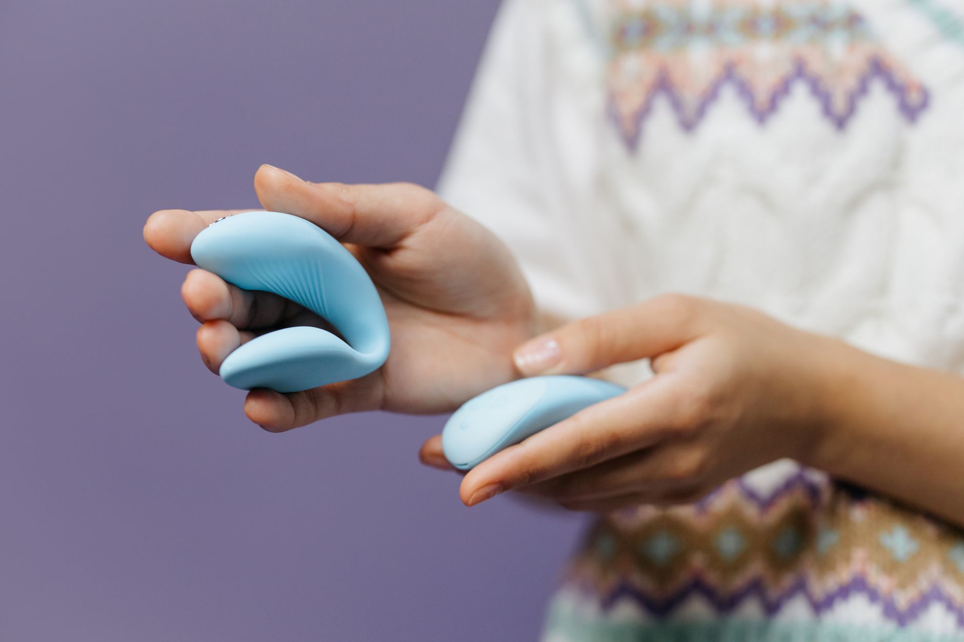 Hand holding a sleek vibrator against a purple background, representing intimate pleasure and modern sensation tools.