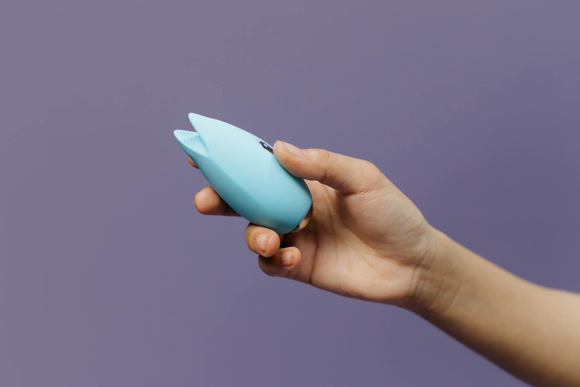 A blue silicone lemon vibrator held in hand against a solid purple background, representing pleasure reclaimed in stolen moments