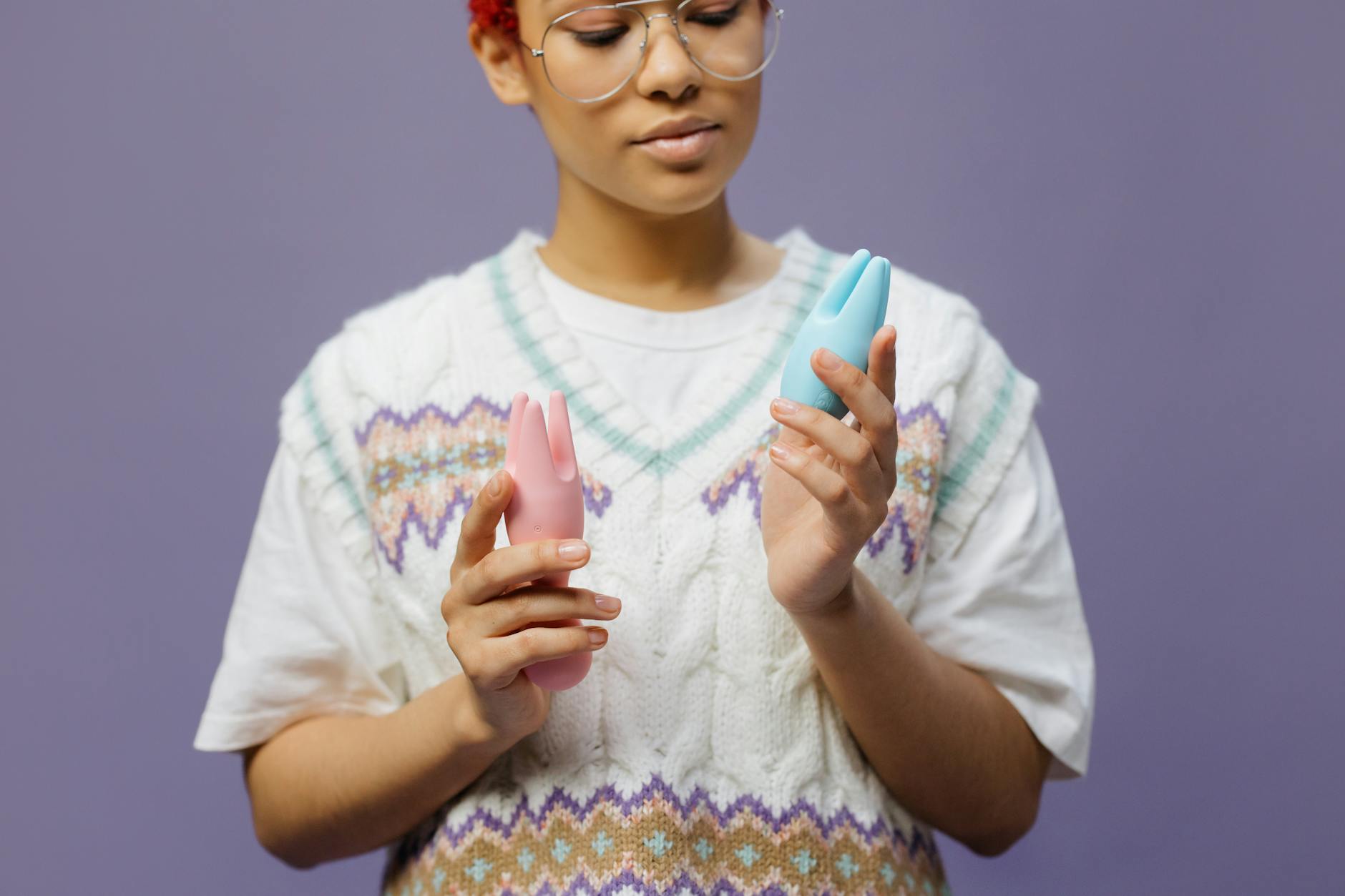 Woman holding blue and pink silicone vibrators in a thoughtful moment during personal pleasure recovery.