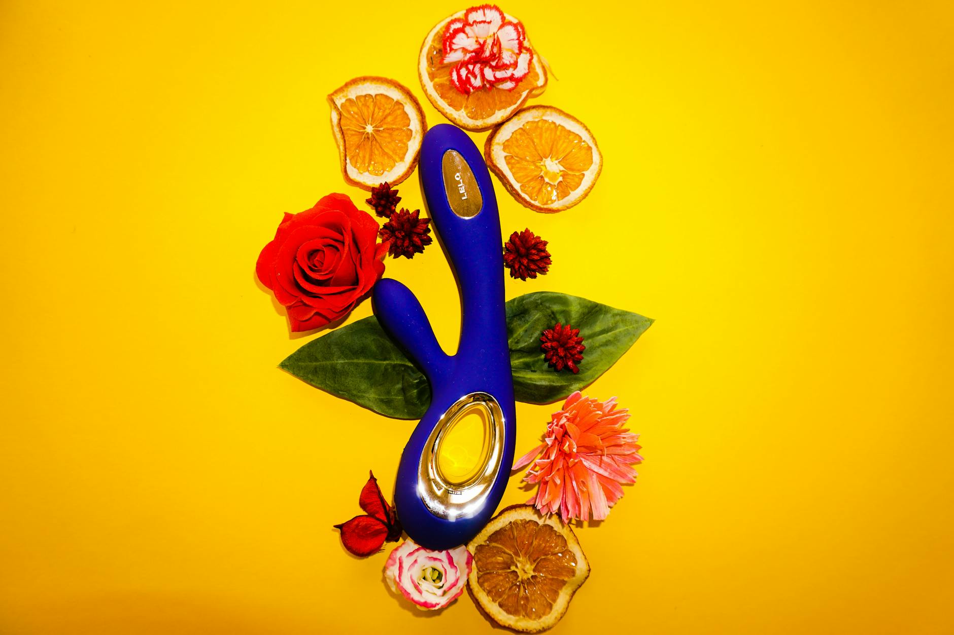 A lemon-colored vibrator surrounded by fresh lemons and flowers on a bright yellow background
